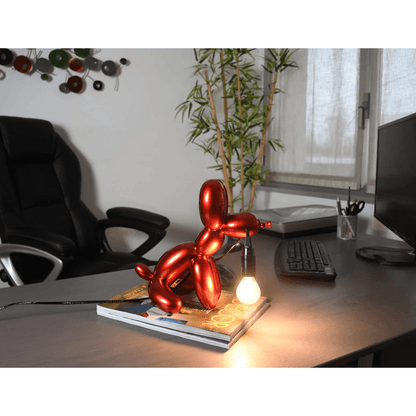 Ballonhund Rot Tischlampe auf einem Schreibtisch, leuchtet sanft und schafft eine künstlerische Atmosphäre im Raum. Skulpturale Pop Art Lampe aus Harz mit Metalleffekt.