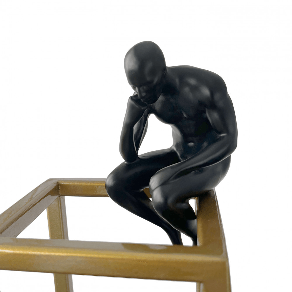 Moderne Figurative Skulptur aus Satinierter Harz mit Chromsockel, Nahaufnahme der sitzenden Figur, die auf dem goldenen Gestell lehnt und in Gedanken versunken wirkt.