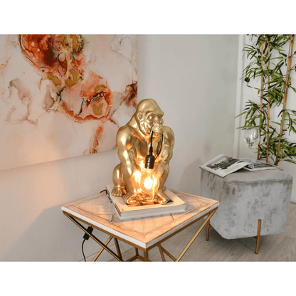 Designer Tischlampe Orang-Utan aus Harz mit Goldeffekt – Installierte Tischlampe auf einem eleganten Tisch, umgeben von stilvollem Wohnambiente.