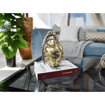 Erleben Sie die Welt der Pop Art mit der einzigartigen Skulptur 'Money Never Sleeps', einer goldenen Granate aus lackiertem Harz, präsentiert auf einem Couchtisch in einem modernen Wohnbereich.