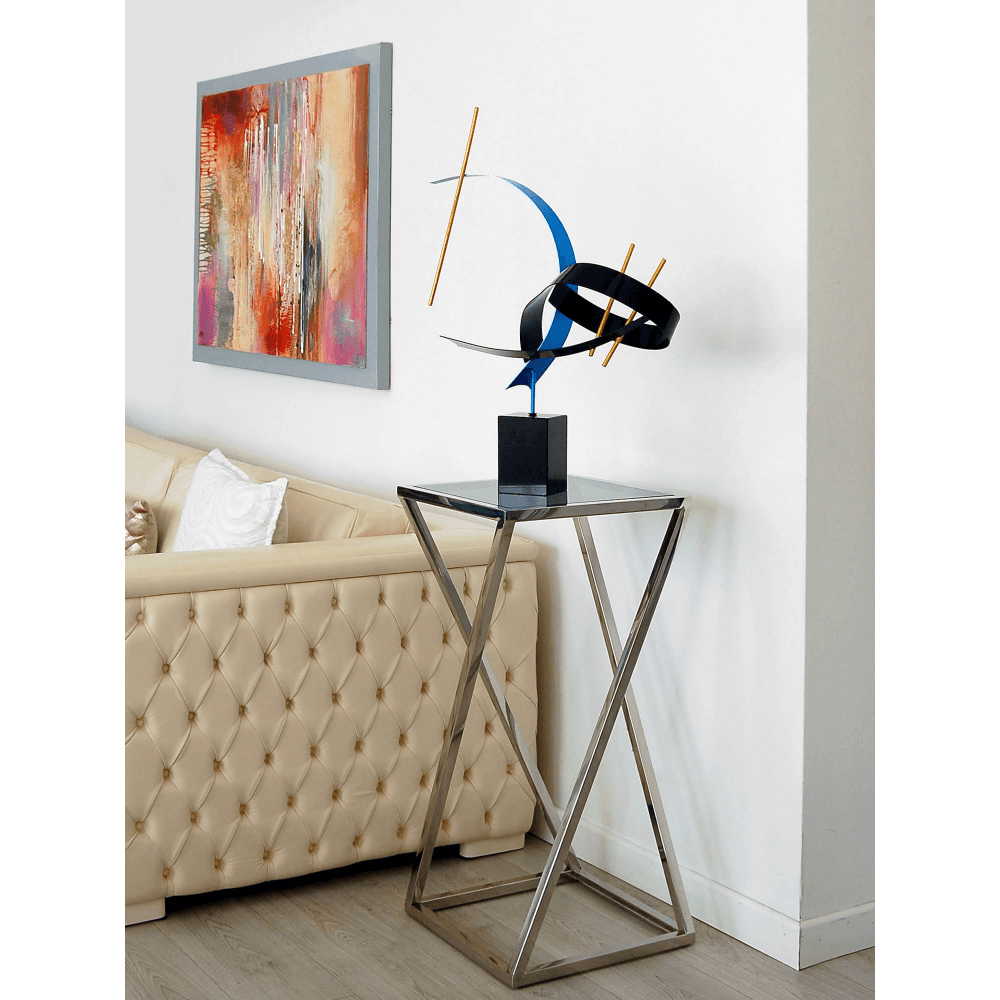 Abstrakte Metallskulptur mit Marmorsockel in leuchtenden Farben, platziert auf einem modernen Tisch in einem stilvollen Wohnraum mit beiger Couch.