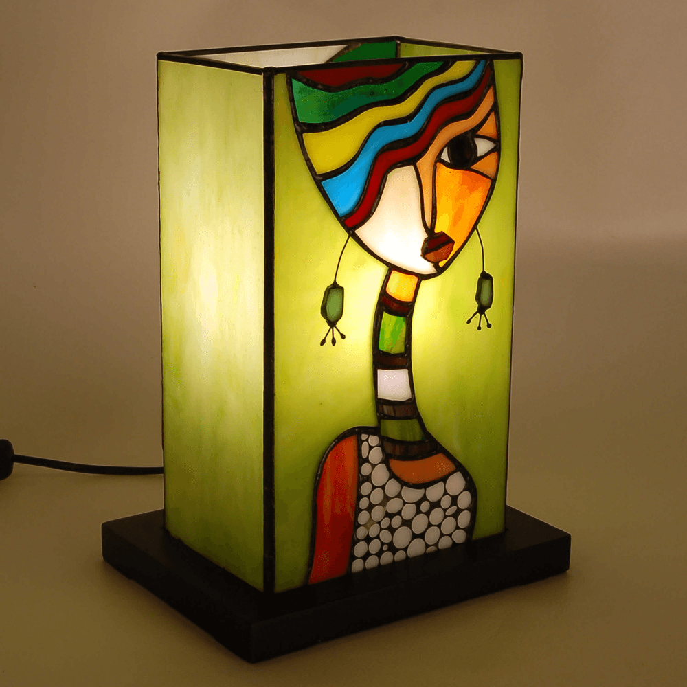 Ästhetisch gestaltete Ethnische Nachttischlampe mit Frauengesicht aus Tiffany-Glas, zeigt farbenfrohes Design auf Abendlicht-Hintergrund.