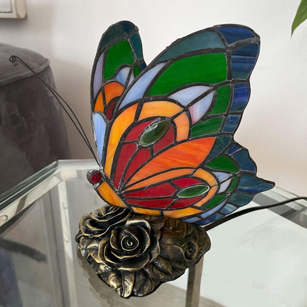 Tiffany Nachttischlampe im Schmetterlingsdesign in lebhaften Farben, von oben betrachtet auf einem Couchtisch, umgeben von natürlichem Licht.