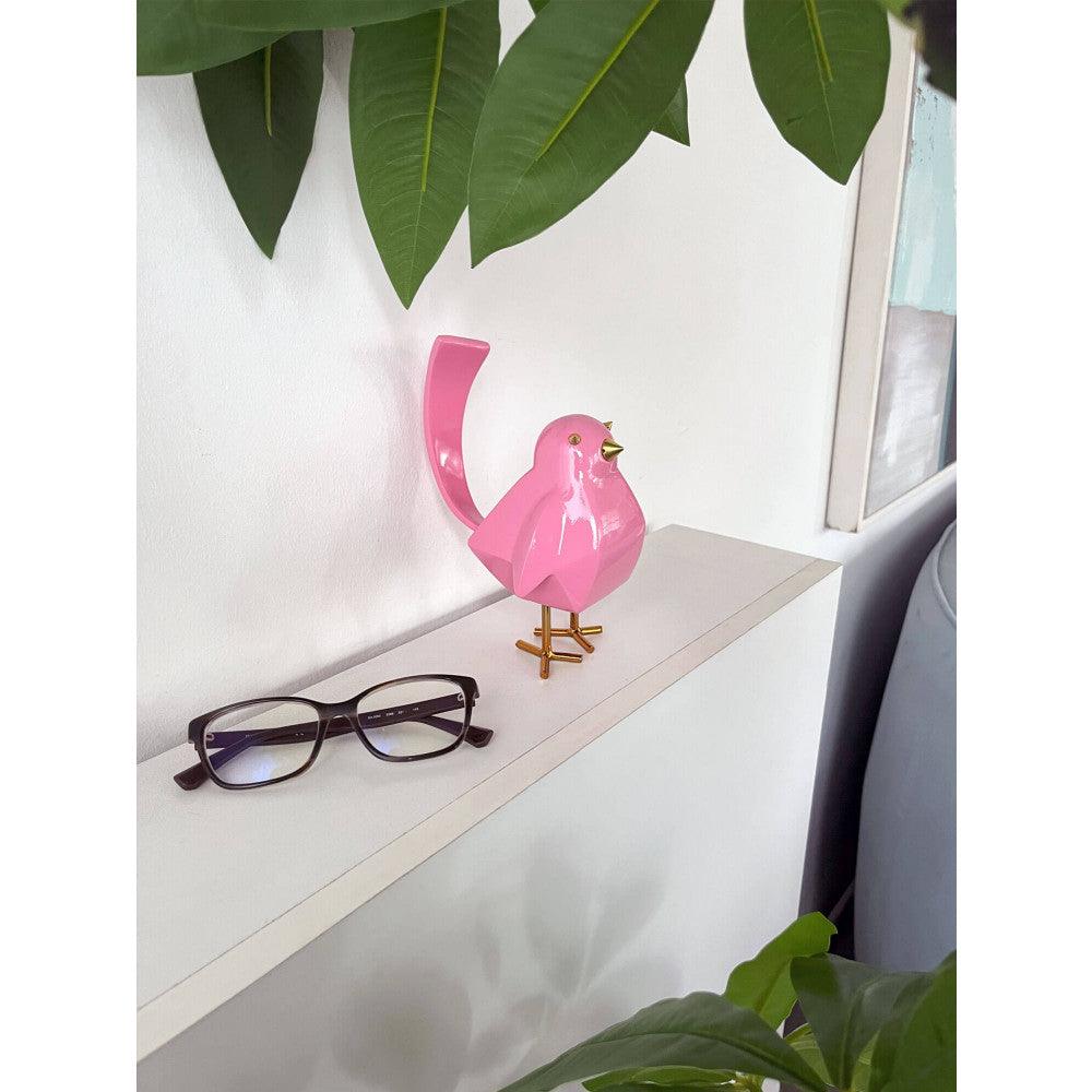 Rosafarbener geometrischer Vogel – Moderne Harzskulptur mit Metalleinsätzen, auf einem Regal platziert mit Brille und Pflanzen, zeigt die dekorative Verwendung.