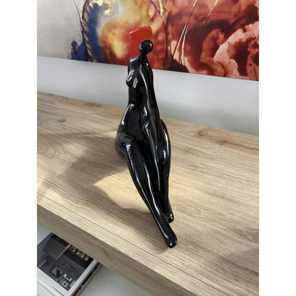 Ruhende Dame – elegante figurative Skulptur in Schwarz aus lackiertem Kunstharz, detailreich und modern, umgeben von einem klaren und minimalistischen Raumdesign.