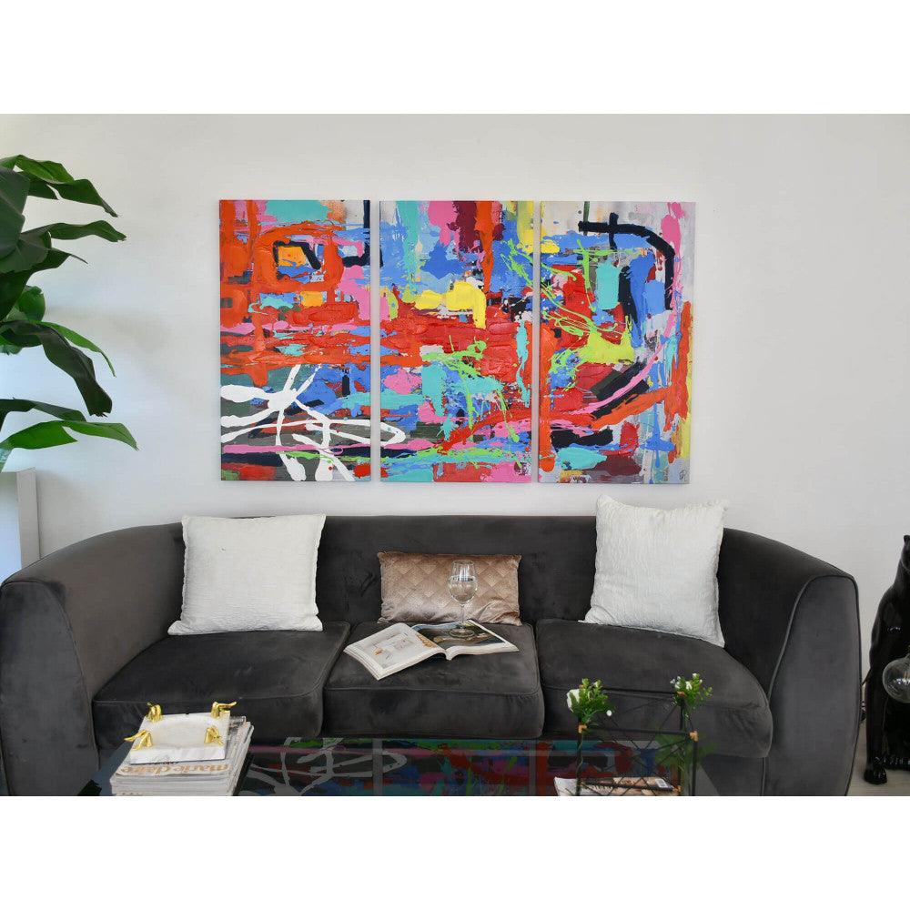 Tris: Abstraktes Kunstwerk mit lebhaften Spritzern auf Leinwand, hängend über einem modernen grauen Sofa, inszeniert in einem zeitgenössischen Wohnzimmer.